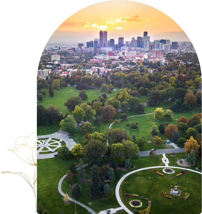 Aerial view of a city skyline at sunset with a large park in the foreground, featuring green spaces, trees, and winding paths. A decorative floral element frames the left edge.