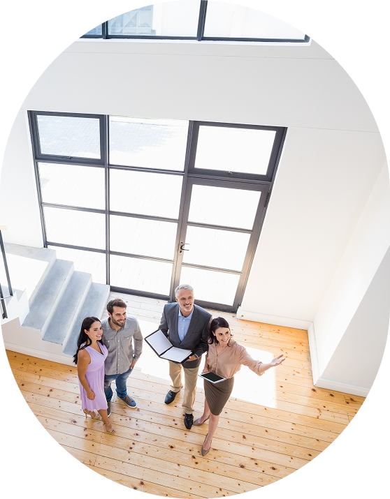 Four people stand in a well-lit room with wooden floors and large windows, holding notebooks and looking upwards.