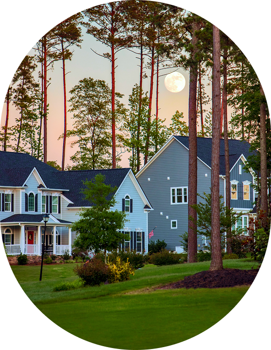 A suburban neighborhood with two houses is shown under a full moon. Tall trees surround the homes, and the sky is a gradient of orange and blue, indicating sunset.