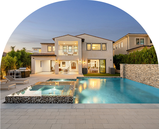Modern two-story house with large windows, lit interior, and an outdoor pool and hot tub on a spacious patio, surrounded by greenery at dusk.